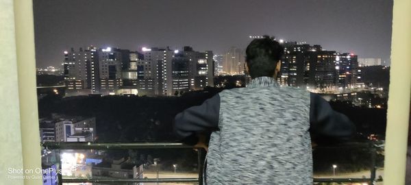 Rear view of man looking at illuminated city buildings