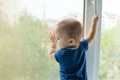 Rear view of boy standing by window