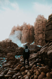 Rear view of man standing on rocks against sky