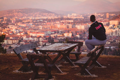 Rear view of man sitting on table against cityscape