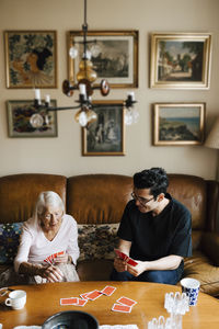 Elderly woman playing cards with male caregiver at table in living room