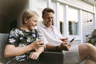 Smiling father sharing smart phone with son while having drinks in back yard