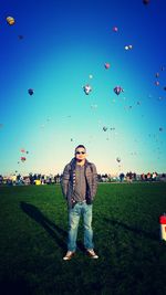 Portrait of man standing on field against hot air balloons in sky