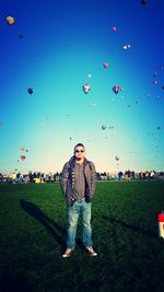 Portrait of man standing on field against hot air balloons in sky