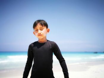 Boy standing on shore at beach against sky during sunny day