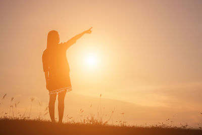 Silhouette woman standing on field against sky during sunset