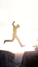 Low angle view of man jumping on rock against sky