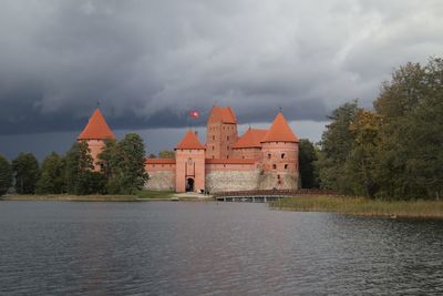 View of castle by river against cloudy sky