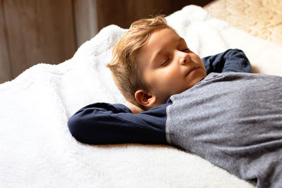 Little boy taking a nap while relaxing with hand behind head in the bedroom.