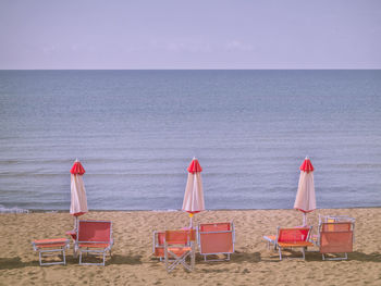 Chairs on beach by sea against sky