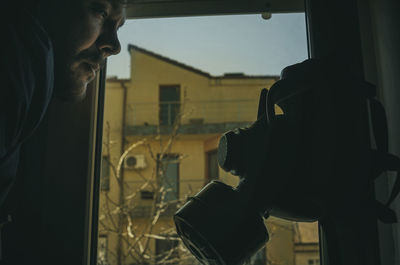 Portrait of young man seen through window facing a teargas mask