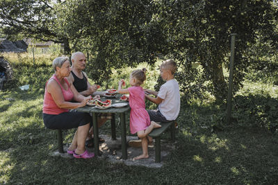Grandparents spending time together with grandson and granddaughter in the garden eating watermelon