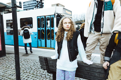 Contemplative girl standing by male friends on footpath in city