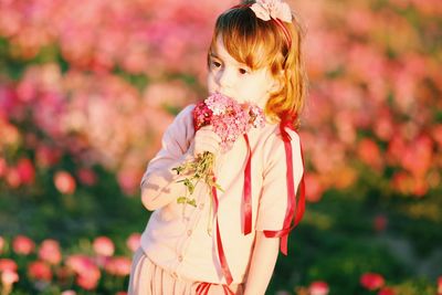 Cute girl with pink flowers standing on land