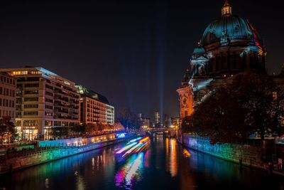 Illuminated buildings by river against sky in city at night