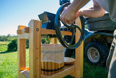 A man turns the flywheel of the apple grinder on a cider press with off road vehicle background 