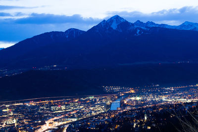 High angle view of illuminated cityscape by mountain at night