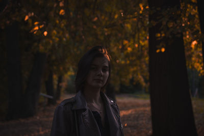 Portrait of young woman standing against trees in forest