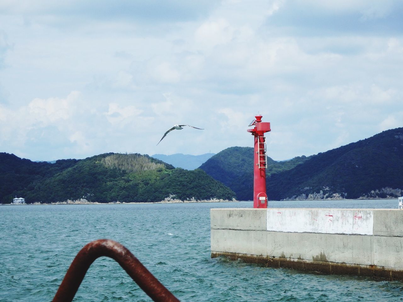 mountain, water, sky, bird, cloud - sky, nature, sea, cloud, built structure, tranquility, day, tranquil scene, mountain range, animal themes, architecture, lake, scenics, outdoors, building exterior, beauty in nature