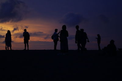 Silhouette people standing on land against sky during sunset