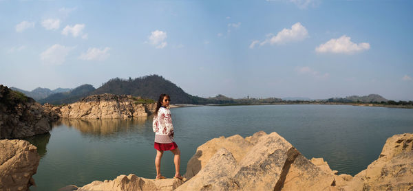 Man standing on rock by mountains against sky