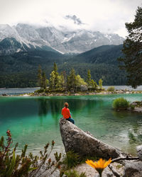 Rear view of woman sitting on rock by lake and mountains