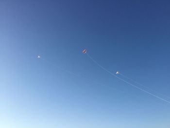 Low angle view of kites flying against clear blue sky