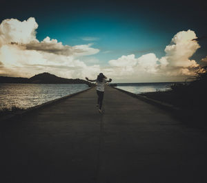Rear view of woman running on pier amidst lake against sky during sunset