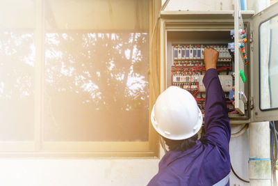 Rear view of worker examining electric box