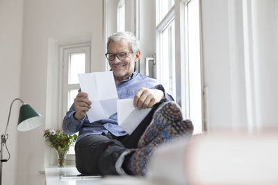 Mature man at home sitting at the window reading documents