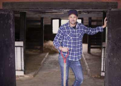 Portrait of confident farmer with pitchfork standing at the entrance of barn