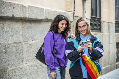 Two friends taking a selfie while walking in the street outdoors with lgbt flag.
