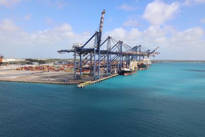 Cranes on pier by sea against sky