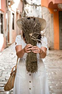 Front view of young woman holding dried lavender bundle in front of her face.
