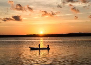 Silhouette men in boat on sea against sky during sunset