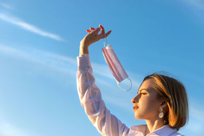 Low angle view of woman holding mask against sky