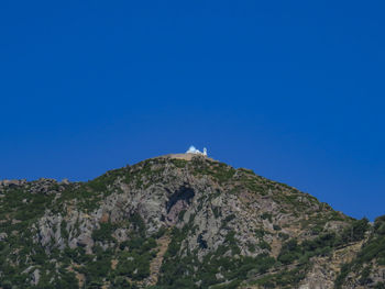 Low angle view of rocky mountain against clear blue sky