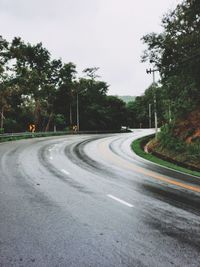 Empty road by trees against sky in city