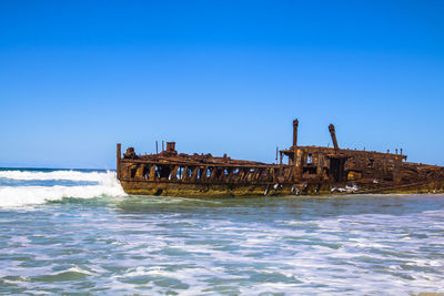 Abandoned ship in sea against clear blue sky