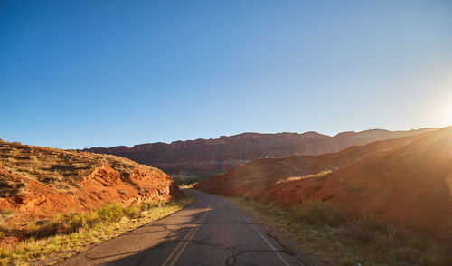 Road leading towards mountains against clear blue sky