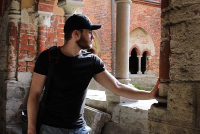 Thoughtful man looking through window while standing at old ruins