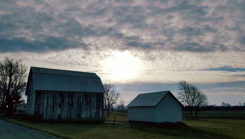 Houses on field against cloudy sky at sunset