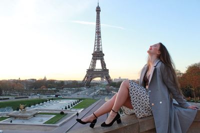 Happy woman sitting on wall with eiffel tower in background