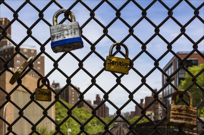 Padlocks on chainlink fence against sky in city