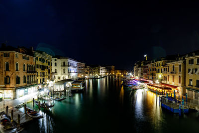 Boats moored on canal amidst buildings in city at night