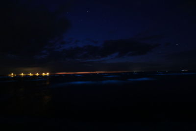 Illuminated lights on beach against sky at night