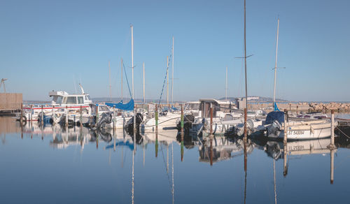 Sailboats moored in harbor against clear blue sky