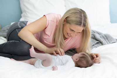 Mother playing with baby girl on bed at home