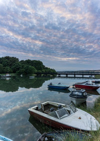 Boats moored in lake against cloudy sky