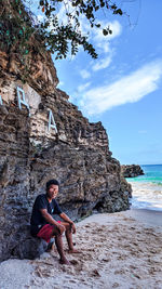 Portrait of young man sitting on beach against sky